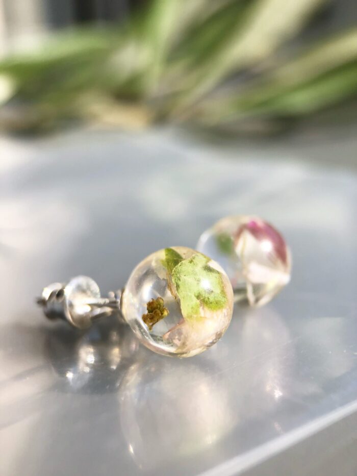 Handgefertigte Ohrstecker Berlin aus Epoxidharz mit zarten weißen und grünen Blüten, 0,8 cm rund, auf reflektierender Oberfläche mit verschwommenem grünem Hintergrund