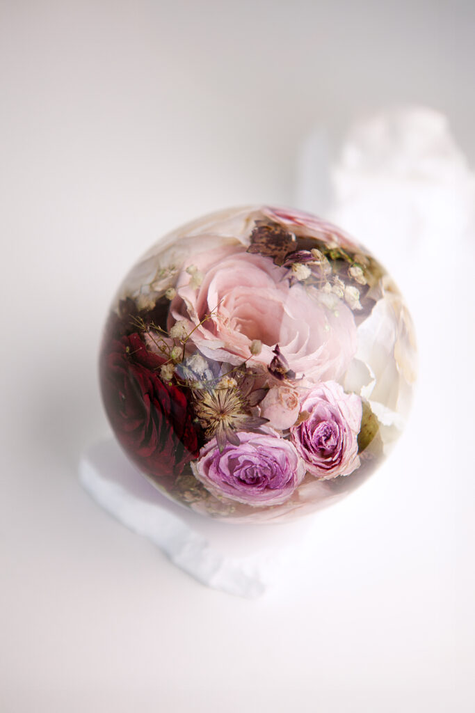 Konservierter Brautstrauß mit lila und weißen Rosen in Epoxidharz-Kugel auf weißem Marmorsockel - Brautstraußkonservierung Flomory