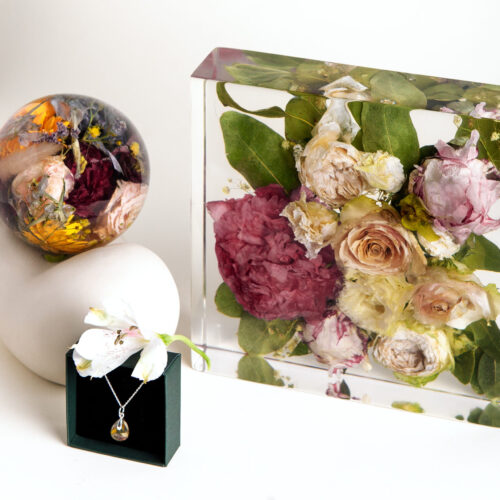 Elegantes Hochzeitserinnerungsset mit konservierten Brautstraußblumen: rechteckiger Kunstharzblock mit rosa Pfingstrosen und cremefarbenen Rosen, dekorative Kunstharzkugel mit bunten Blütenakzenten und passender Schmuckanhänger auf schwarzer Schmuckbox, alles auf weißem Hintergrund arrangiert