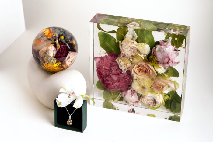 Elegantes Hochzeitserinnerungsset mit konservierten Brautstraußblumen: rechteckiger Kunstharzblock mit rosa Pfingstrosen und cremefarbenen Rosen, dekorative Kunstharzkugel mit bunten Blütenakzenten und passender Schmuckanhänger auf schwarzer Schmuckbox, alles auf weißem Hintergrund arrangiert