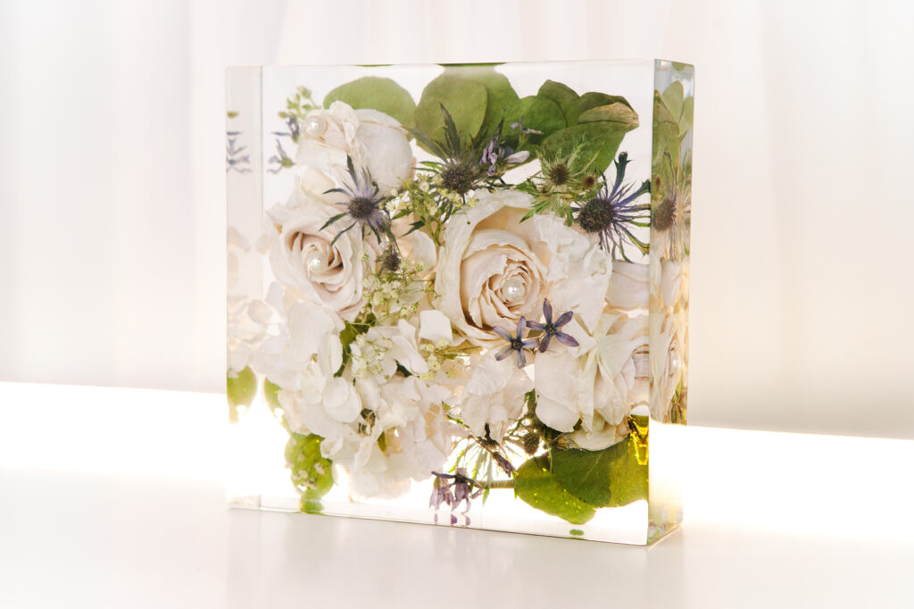 Gefriergetrockneter Brautstrauß in quadratischem Resin-Block mit weißen Gartenrosen mit Perlen, blauen Disteln, weißen Hortensien und grünem Blattwerk in kristallklarem Harz