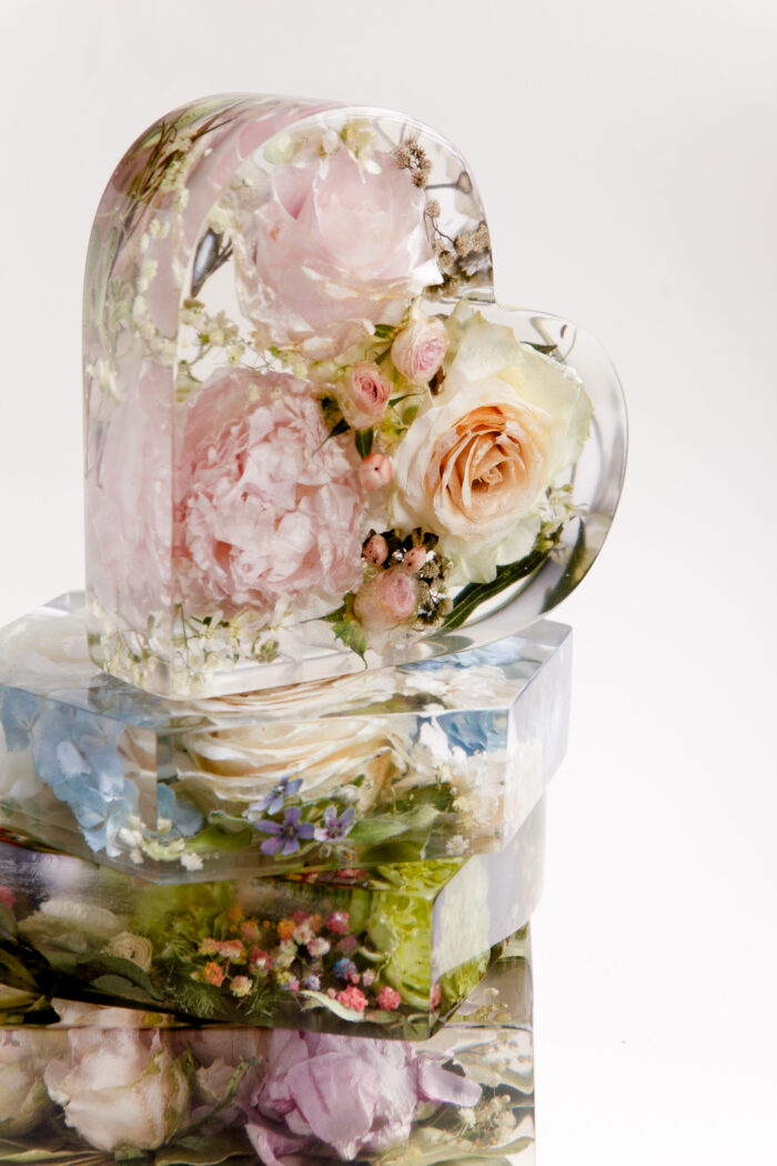 Eleganter herzförmiger Kunstharz-Block mit konservierten Brautstraußblumen in Pastelltönen, gefüllt mit rosa Pfingstrosen, cremefarbenen Rosen und zarten Miniatur-Rosenblüten, auf rechteckigen Kunstharz-Blöcken mit weiteren Hochzeitsblumen gestapelt, zeitlose Hochzeitserinnerung als stilvolle Dekoration