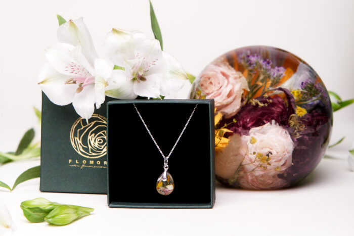 Silberkette mit Brautstraußblüten-Anhänger in edler Geschenkbox neben Acrylkugel mit konservierten Hochzeitsblumen