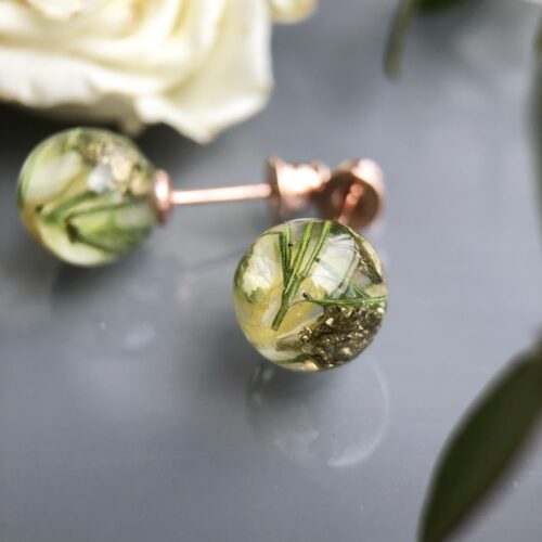 Handgefertigte Ohrstecker aus Epoxidharz mit zarten weißen und grünen Blüten, 0,8 cm rund, auf reflektierender Oberfläche mit verschwommenem grünem Hintergrund