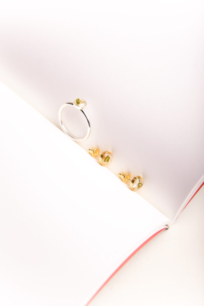Elegantes Schmuckset "London" bestehend aus goldenen Ohrsteckern und einem silbernen Ring, jeweils mit in Kunstharz eingebetteten grünen Blättern aus einem Brautstrauß, arrangiert neben getrockneten Schleierkrautblüten auf cremefarbenem Untergrund.