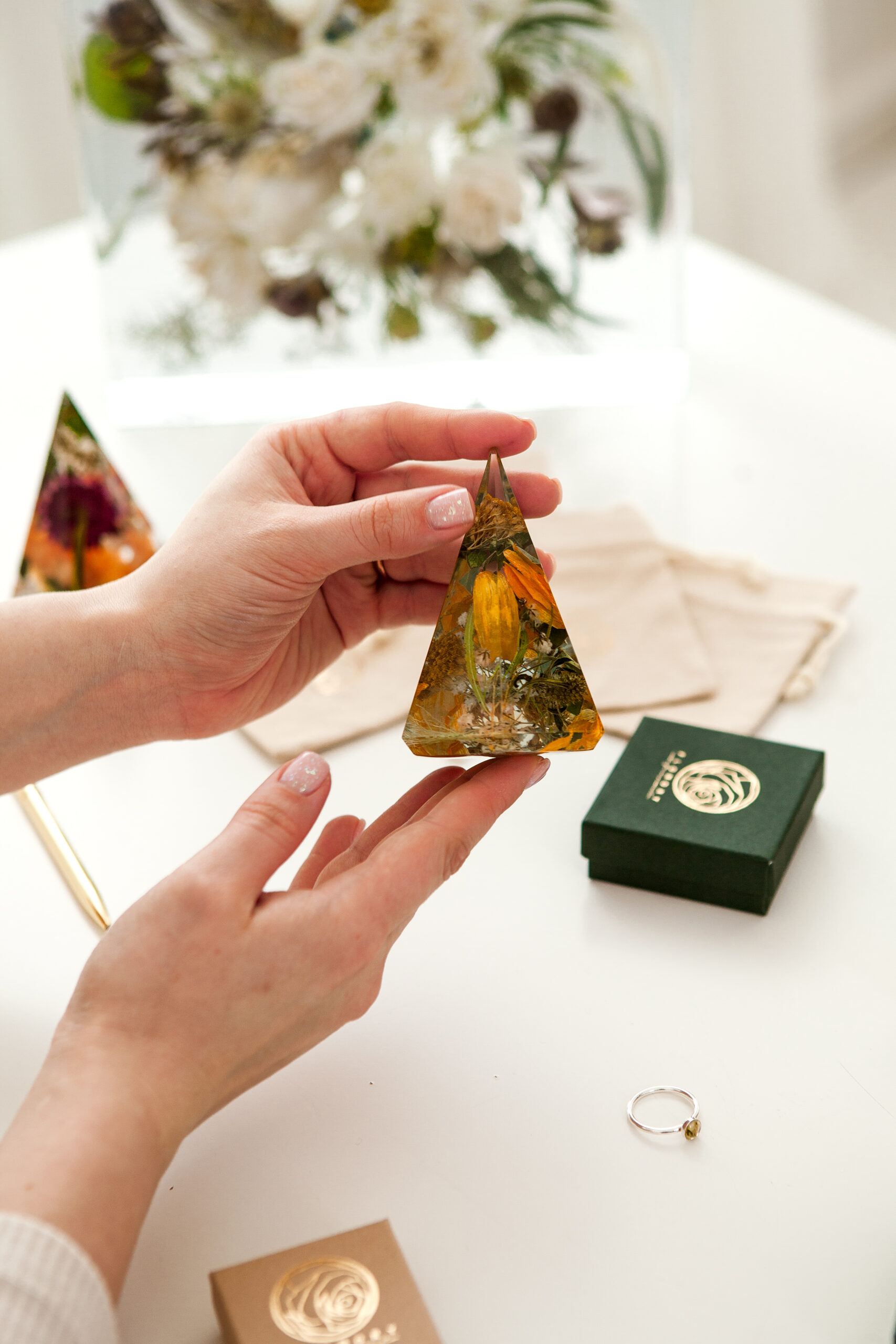 Präsentation einer pyramidenförmigen Brautstraußkonservierung mit orangefarbenen Blüten neben Markenverpackung und Schmuckring