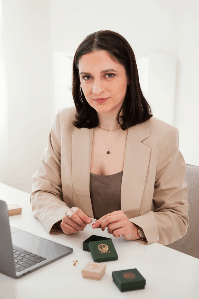 Expertin für Brautstraußkonservierung präsentiert handgefertigten Erinnerungsschmuck in eleganten Schmuckboxen. Die Designerin im beigen Blazer zeigt, wie Hochzeitsblüten in wertvolle Schmuckstücke transformiert werden - ein persönliches Andenken an den besonderen Tag.