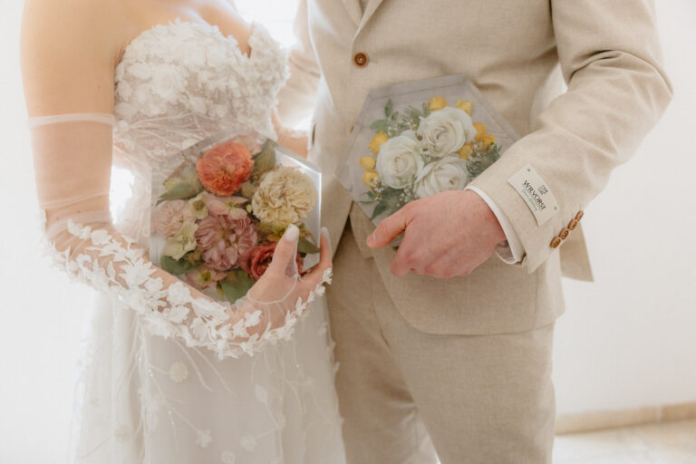 Brautpaar hält konservierte Hochzeitssträuße in Acrylboxen - links pastellfarbene Blüten der Braut, rechts weiße Rosen des Bräutigams