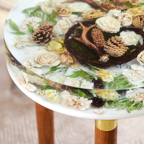 Perspektivische Ansicht Brautstraußtisch in Harz - cremefarbene Rosen, Kiefernzapfen und Farn in transparenten Schichten, Holzbeine mit Golddetail - Premium Flomory