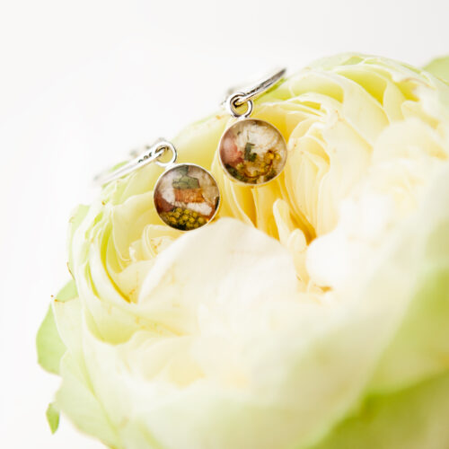 Silberne Ohrhänger mit runden Resin-Anhängern aus gefriergetrockneten Brautblumen, drapiert auf einer weißen Pfingstrose