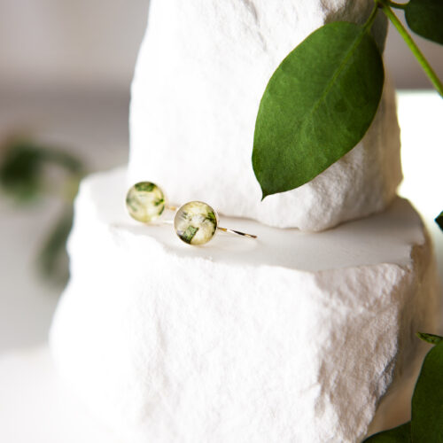 Goldene Ohrhänger Lissabon mit rundem Resin-Anhänger aus gefriergetrockneten Brautblumen in Grün und Weiß, auf weißem Stein mit Eukalyptus – Nahaufnahme von oben